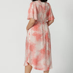 Back view of a good dress for petite women, this silky flutter sleeve dress in viscose fabric has an orange spot print. Made in Australia by women's clothes label, Leina & Fleur, this lightweight summer dress is breathable. Shop this summer wedding guest and event wear outfit online in sizes 8 to 24.