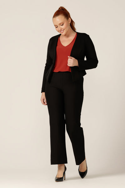 A classic workwear jacket, the Yuri Jacket in Black is a collarless, open-front, soft tailored jacket. Shown here in a size 12, the jacket is worn with black tailored pants to create a work suit look, and a V-neck top in orange. All are made in Australia by Australian and New Zealand women's clothing label, L&F. 