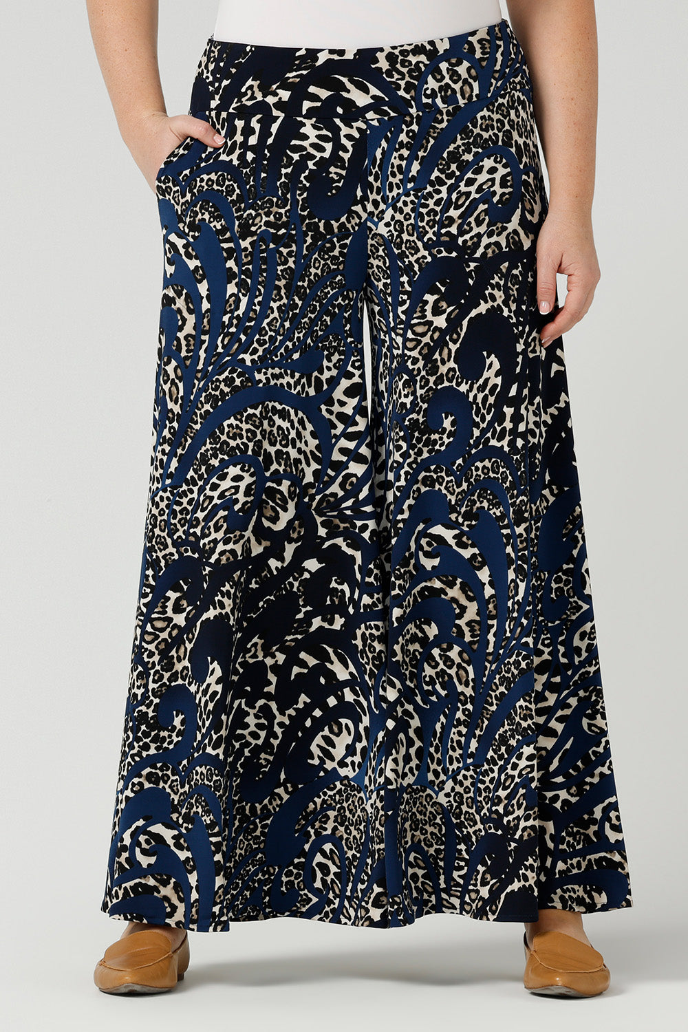Close up of A curvy size, size 12 woman wears printed wide leg pants with pockets with a navy round neck top. These pull-on, easy care pants are comfortable for your everyday workwear capsule wardrobe. Shop these Australian-made wide leg trousers online in sizes 8 to 24, petite to plus sizes.