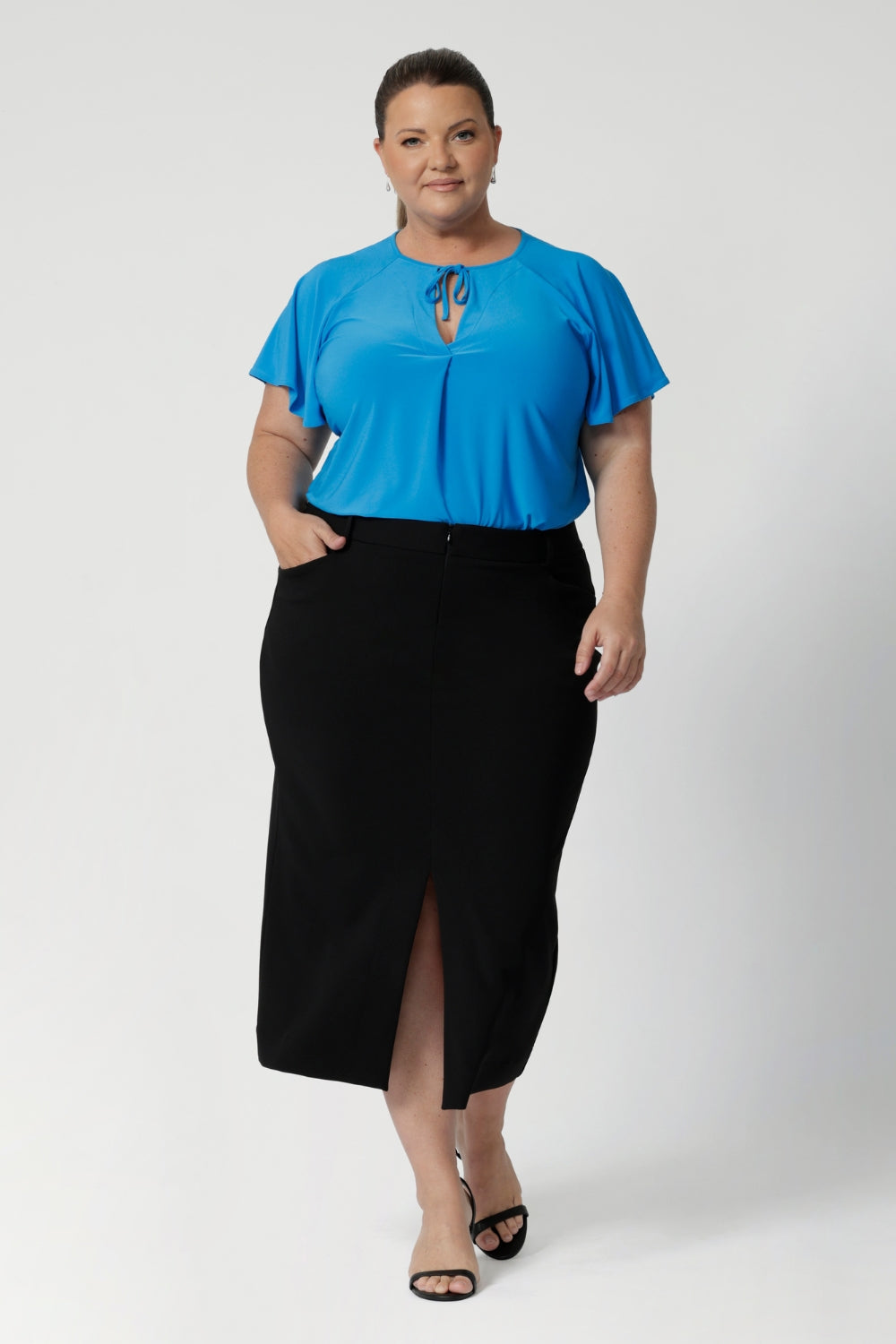 Australian made black workwear skirt seen on over 40's woman paired with opal coloured shirt and black heels for an elevated workwear look. Sizes 8-24 available at Leina & Fleur.