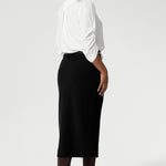Back view image of Australian made black workwear skirt seen on over 30's woman paired with white blouse and brown boots for an elevated workwear look. Sizes 8-24 available at Leina & Fleur.