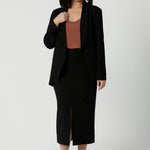 Petite height model wears straight-cut black midi skirt in lightweight scuba crepe jersey, designed by Australian and New Zealand women's clothing brand, Leina & Fleur. This stretchy, easy-care skirt is a perfect skirt for petite women, an ideal as both a workwear skirt and off duty skirt.
