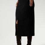 Close up image of Made in Australia by Australian and New Zealand women's clothing brand, Leina & Fleur. This stretchy, easy-care skirt is a perfect workwear piece for elevated suit styling with matching jacket or blazer. Size 10 model wears her midi length workwear skirt with long boots and a white collared blouse.