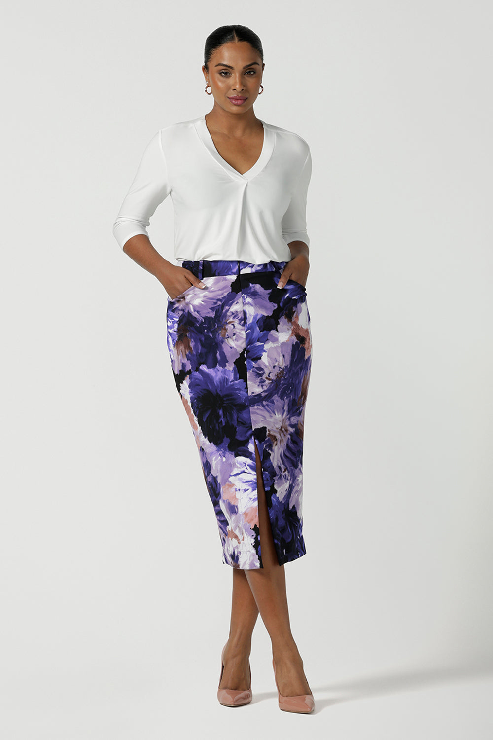 A size 10 woman wears the Aaron Midi Skirt in Jacaranda. A printed Midi length skirt in purple florals. Made in Australia for women size 8-24. Styled back with pink pumps and a purple Jacaranda jacket.