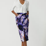 A size 10 woman wears the Aaron Midi Skirt in Jacaranda. A printed Midi length skirt in purple florals. Made in Australia for women size 8-24. Styled back with pink pumps and a purple Jacaranda jacket.