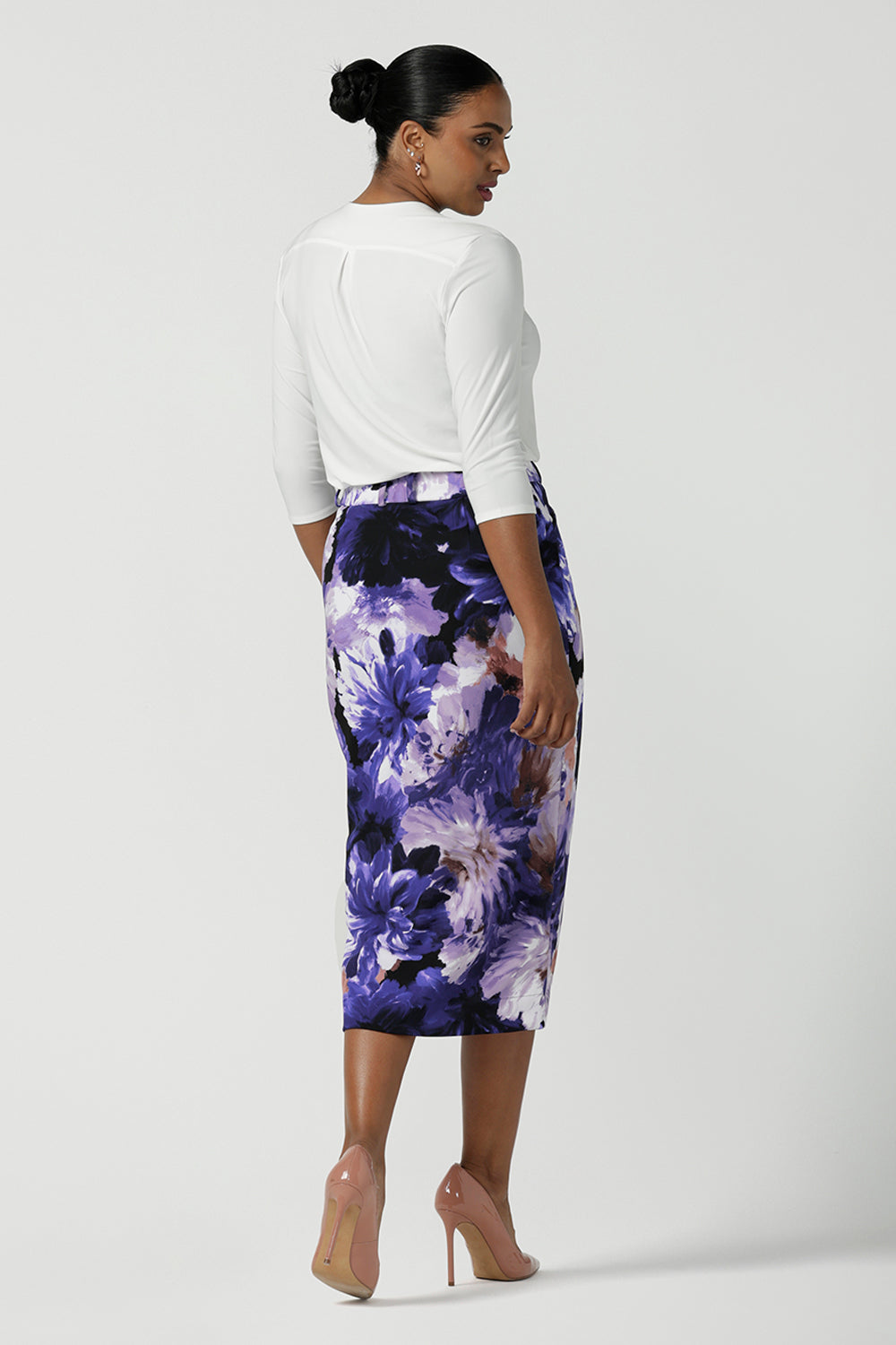 Back view of a size 10 woman wearing the Aaron Midi Skirt in Jacaranda. A printed Midi length skirt in purple florals. Made in Australia for women size 8-24. Styled back with pink pumps and a purple Jacaranda jacket.