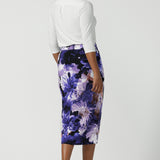 Back view of a size 10 woman wearing the Aaron Midi Skirt in Jacaranda. A printed Midi length skirt in purple florals. Made in Australia for women size 8-24. Styled back with pink pumps and a purple Jacaranda jacket.