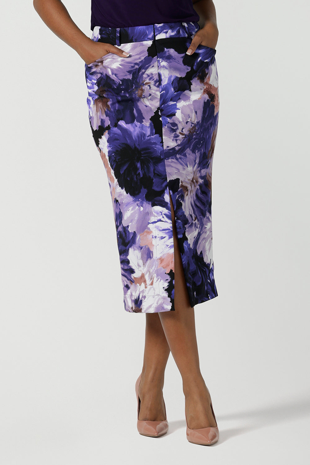 Close up of a size 10 woman wears the Aaron Midi Skirt in Jacaranda. A printed Midi length skirt in purple florals. Made in Australia for women size 8-24. Styled back with pink pumps. 