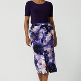 A size 10 woman wears the Aaron Midi Skirt in Jacaranda. A printed Midi length skirt in purple florals. Made in Australia for women size 8-24. 