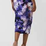 Back view of a size 10 woman wears the Aaron Midi Skirt in Jacaranda. A printed Midi length skirt in purple florals. Made in Australia for women size 8-24. Styled back with pink pumps.