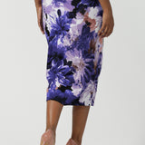 Back view of a size 10 woman wears the Aaron Midi Skirt in Jacaranda. A printed Midi length skirt in purple florals. Made in Australia for women size 8-24. Styled back with pink pumps.