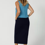 Full body back view of size 12 model wearing midi length skirt. Workwear skirt is made from easy care scuba crepe fabric. Workwear skirt has a deep navy colour. This comfortable midi skirt provides full body stretch great for any office or corporate setting. Australian  made clothing by Australian and New Zealand women. Leina and Fleur is a woman’s fashion label that stocks sizes from 8 to 24. Shop this navy skirt in plus size and petite sizes. 