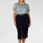 Full body front view of 40 year old plus sized woman wearing a midi length work skirt. This workwear skirt is navy in colour and made of good quality scuba crepe fabric. This skirt has an above the knee slit for comfort and mobility. Perfect skirt for an office or corporate setting. 3/4 length skirt is Australia made by New Zealand and Australian women. Leina & Fleur is a clothing company for woman that stock sizes from 8 to 24. Shop this work skirt in plus sizes and petite sizes. 