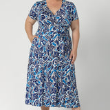 Plus size model wears short sleeve dress, designed with delicate tucks on the shoulder, midi length skirt & full wrap design. From workday sophistication to event-ready weekend comfort. This dress is built on a slinky jersey base, offering a soft, stretchable fit that moves with everybody to ensure comfort and style. Available in sizes 8-24.