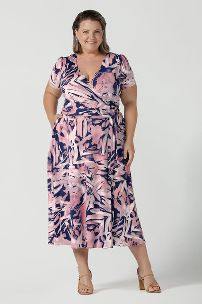 A size 18 Curvy woman wears the Alexis dress in the Cantata print. A functioning wrap dress with tie side and short sleeve and midi length. Navy base with an abstract brush strokes leafy print. Made in Australia for women size inclusive 8 - 24.