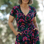 Featuring a striking floral print in bold shades of pink, green, burgundy, and blue, this dress flatters with its true wrap silhouette, extended waist ties, and a flowing A-line skirt.