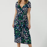 A size 12 woman wears the Alexis jersey wrap dress in navy blue, green and white print. An easy-care work dress for everyday office and corporate wear, in sizes 8 to 24 this is a good plus size dress. Made in Australia by Australian and New Zealand women's clothes brand, Leina & Fleur, this wrap dress is part of a collection of dresses for plus size to petite height women.  