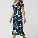 A size 12 woman wears a short sleeve, jersey wrap dress in navy blue, green and white print. Available to shop in sizes 8 to 24 this is a great curve work dress for plus size women.  Made in Australia by Australian and New Zealand women's clothes brand, Leina & Fleur, this wrap dress is part of a collection of dresses for plus size to petite height women.  