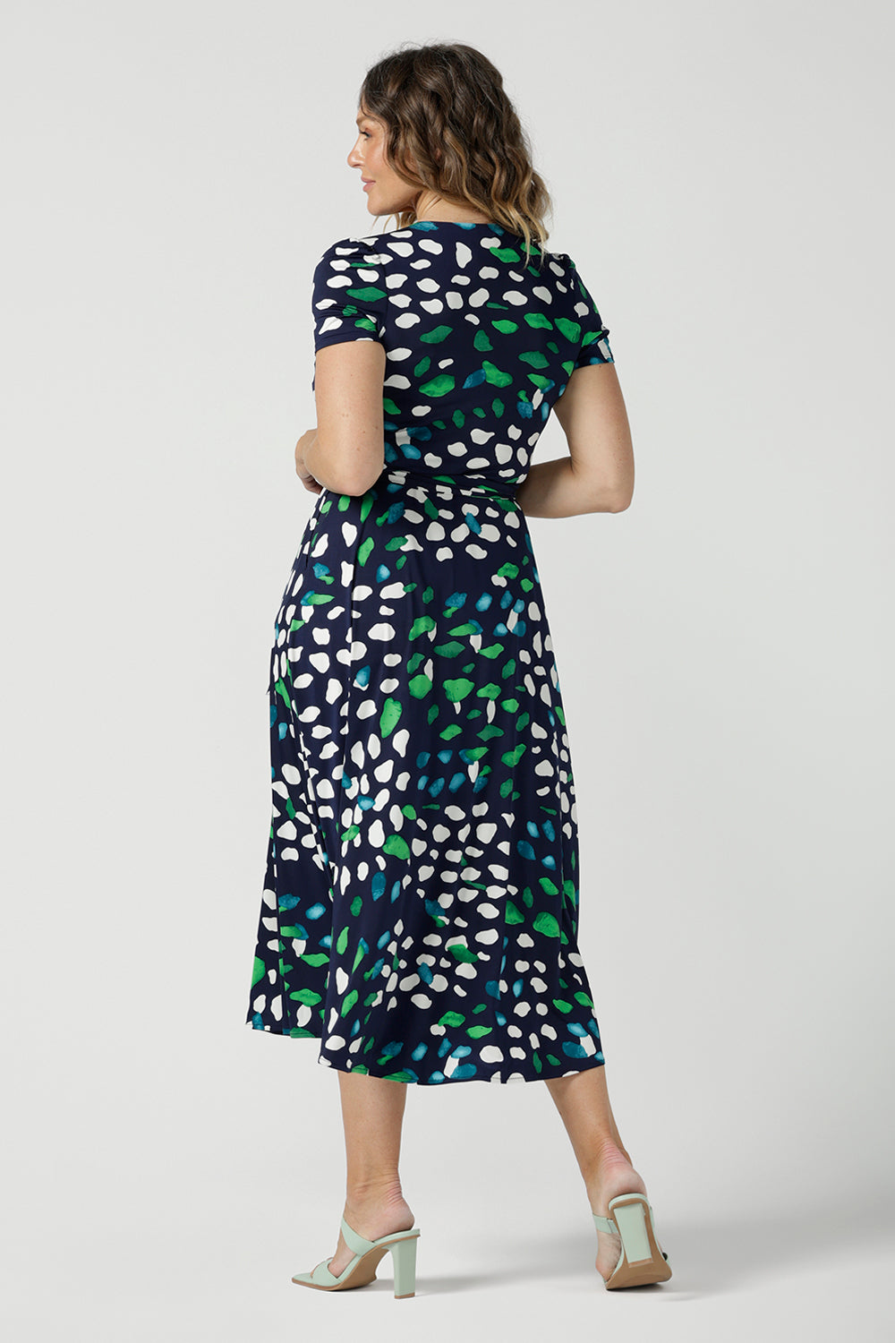 Back view of a size 12 woman wearing a jersey wrap dress in navy blue, green and white print. An easy-care work dress for everyday office and corporate wear, in sizes 8 to 24 this is a good plus size dress. Made in Australia by Australian and New Zealand womens clothing label, Leina & Fleur, this wrap dress is part of a collection of dresses for plus size to petite height women.  