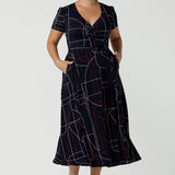 Size 12 corporate woman wears the Alexis dress in Navy Abstract. A functioning wrap dress in comfortable jersey material. Midi length with short sleeves. A geometric pattern with red and white on a navy base. Made in Australia for women size 8 - 24.
