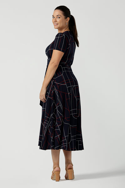 Size 12 corporate woman wears the Alexis dress in Navy Abstract. A functioning wrap dress in comfortable jersey material. Midi length with short sleeves. A geometric pattern with red and white on a navy base. Made in Australia for women size 8 - 24.