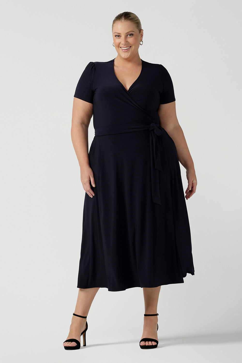 A curvy, size 18 woman wearing a navy, wrap dress with short sleeves. A great dress for summer casual wear, or for travel. Shop made in Australia dresses in petite to plus sizes online at Australian fashion brand, Leina & Fleur.