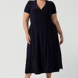 A curvy, size 18 woman wearing a navy, wrap dress with short sleeves. A great dress for summer casual wear, or for travel. Shop made in Australia dresses in petite to plus sizes online at Australian fashion brand, Leina & Fleur.