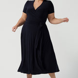 A curvy, size 18 woman wearing a navy, wrap dress with short sleeves. A great dress for summer casual wear, or for travel. Shop made in Australia dresses in petite to plus sizes online at Australian fashion brand, Leina & Fleur.