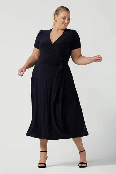 A curvy, size 18 woman wearing a navy, wrap dress with short sleeves. A great dress for summer casual wear, or for travel. Shop made in Australia dresses in petite to plus sizes online at Australian fashion brand, Leina & Fleur.