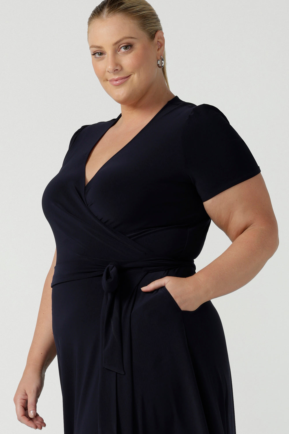 Close up of a curvy, size 18 woman wearing a navy, wrap dress with short sleeves. A great dress for summer casual wear, or for travel. Shop made in Australia dresses in petite to plus sizes online at Australian fashion brand, Leina & Fleur.