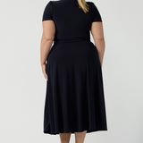 Back view of a curvy, size 18 woman wearing a navy, wrap dress with short sleeves. A great dress for summer casual wear, or for travel. Shop made in Australia dresses in petite to plus sizes online at Australian fashion brand, Leina & Fleur.