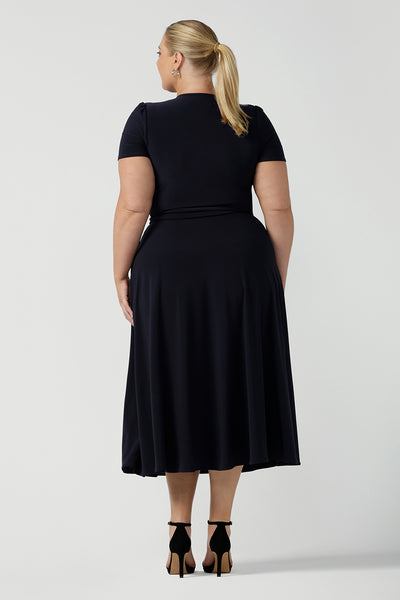 Back view of a curvy, size 18 woman wearing a navy, wrap dress with short sleeves. A great dress for summer casual wear, or for travel. Shop made in Australia dresses in petite to plus sizes online at Australian fashion brand, Leina & Fleur.