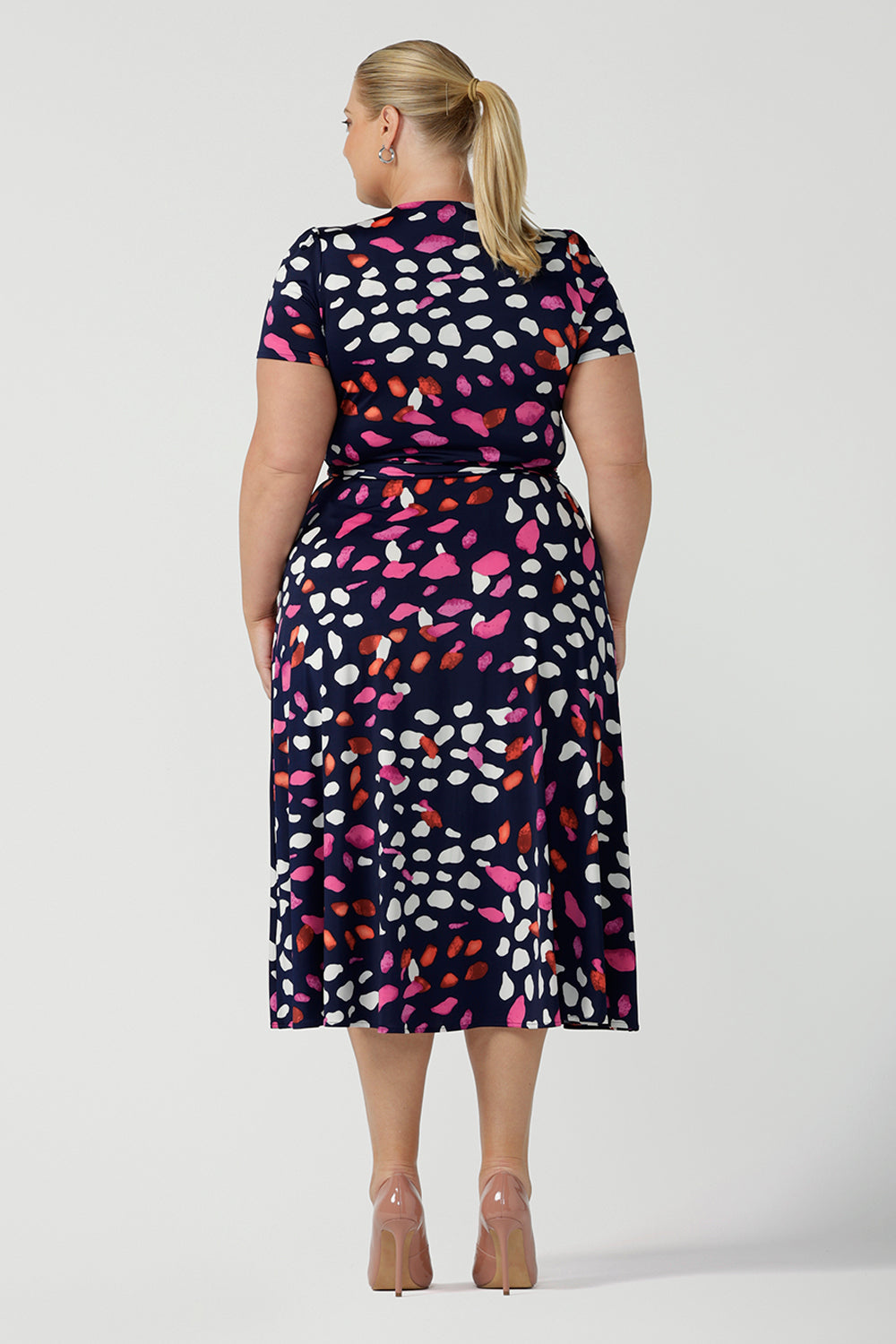 Back view of a curvy, size 18 woman wearing an abstract jersey print, wrap dress with short sleeves. A great dress for summer casual wear, or for travel. Shop made in Australia dresses in petite to plus sizes online at Australian fashion brand, Leina & Fleur.