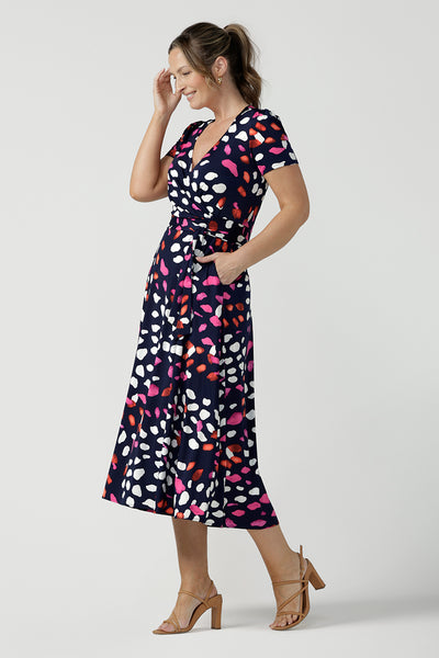 An over 40, size 10 woman wearing a abstract jersey print, wrap dress with short sleeves. A great dress for summer casual wear, or for travel. Shop made in Australia dresses in petite to plus sizes online at Australian fashion brand, Leina & Fleur.