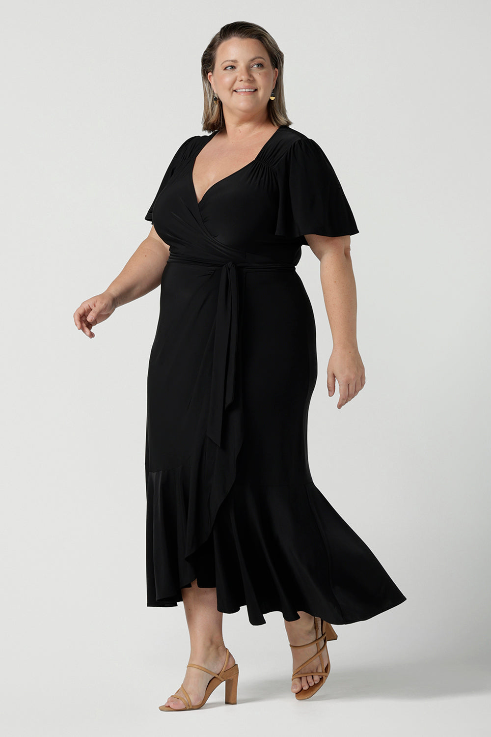 Size 18 woman wears a Alita dress in black. An elegant wrap dress with a tier and sweetheart neckline and flutter sleeve. Made in Australia for women size 8 - 24.