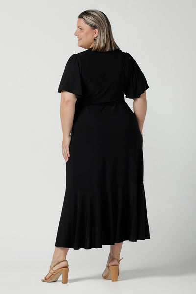 Back view of a size 18 woman wears a Alita dress in black. An elegant wrap dress with a tier and sweetheart neckline and flutter sleeve. Made in Australia for women size 8 - 24.