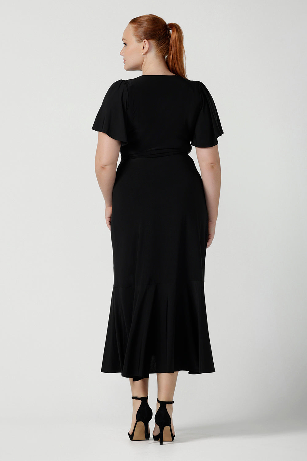 Back view of a size 12 woman wears a Alita dress in black. An elegant wrap dress with a tier and sweetheart neckline and flutter sleeve. Made in Australia for women size 8 - 24.