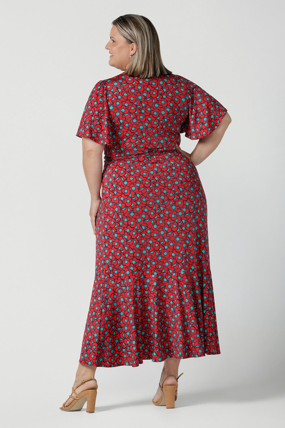 Back view of a curvy woman wearing a size 18 woman wearing a wrap dress in soft slinky jersey. The beautiful Rio print has seventies inspired florals with aqua.Romantic valentines day dressing, frill hem and flutter sleeve for curvy women size 8 - 24.
