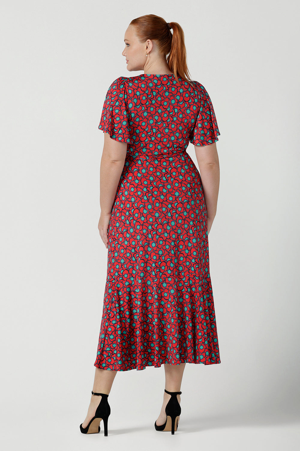 Back view of a size 12 curvy woman wearing a size 12 wrap dress in soft slinky jersey. The beautiful Rio print has seventies inspired florals with aqua.Romantic valentines day dressing, frill hem and flutter sleeve for curvy women size 8 - 24.