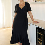 Alita Wrap Dress in Black — elegant slinky jersey wrap dress with flutter sleeves and ruffled hem, perfect for party season glamour.