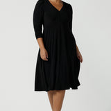 Size 16 woman wears a Alyssa Dress in jersey. V-neckline style great for work to weekend wear. Corporate dress for women. Travel friendly with an empire line style. Midi dress and styled back with black strappy heels. Made in Australia for women size 8 - 24.