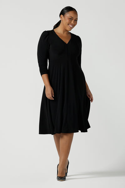Size 16 woman wears a Alyssa Dress in jersey. V-neckline style great for work to weekend wear. Corporate dress for women. Travel friendly with an empire line style. Midi dress and styled back with black strappy heels. Made in Australia for women size 8 - 24.