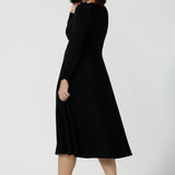 Back view of size 10 Alyssa Dress in jersey. V-neckline style great for work to weekend wear. Corporate dress for women. Travel friendly with an empire line style. Midi dress and styled back with black strappy heels. Made in Australia for women size 8 - 24.