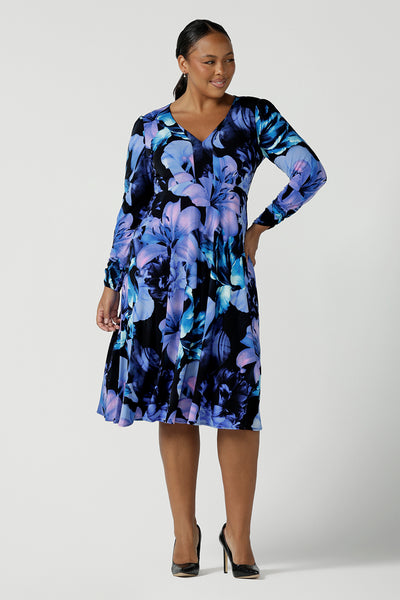 Size 16 woman wears the Alyssa Dress in Blue Lily, Empire line style with bold blue flowers on a black base. Deep V - neckline and size inclusive. Made in Australia for women size 8 - 24.