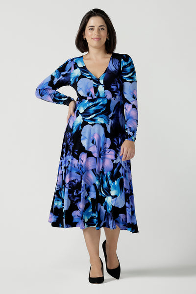 Size 10 woman wears the Alyssa Dress in Blue Lily, Empire line style with bold blue flowers on a black base. Deep V - neckline and size inclusive. Made in Australia for women size 8 - 24.