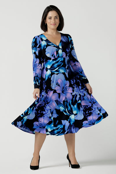 Close up of a Size 10 woman wears the Alyssa Dress in Blue Lily, Empire line style with bold blue flowers on a black base. Deep V - neckline and size inclusive. Made in Australia for women size 8 - 24. Petite to plus size women. Dresses for workwear to event dressing.