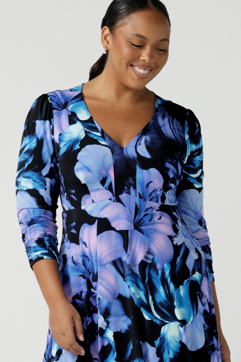 Close up of a size 16 woman wears the Alyssa Dress in Blue Lily, Empire line style with bold blue flowers on a black base. Deep V - neckline and size inclusive. Made in Australia for women size 8 - 24.