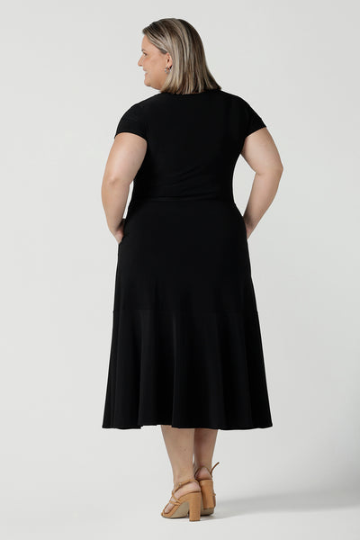 Back view of a size 18 woman wears the Amal dress in black is a slim fit round neck dress with waist seam and tier at the bottom. Functioning pockets. Great for work or event occasions. Made in Australia. Size inclusive fashion for women size 8 - 24.