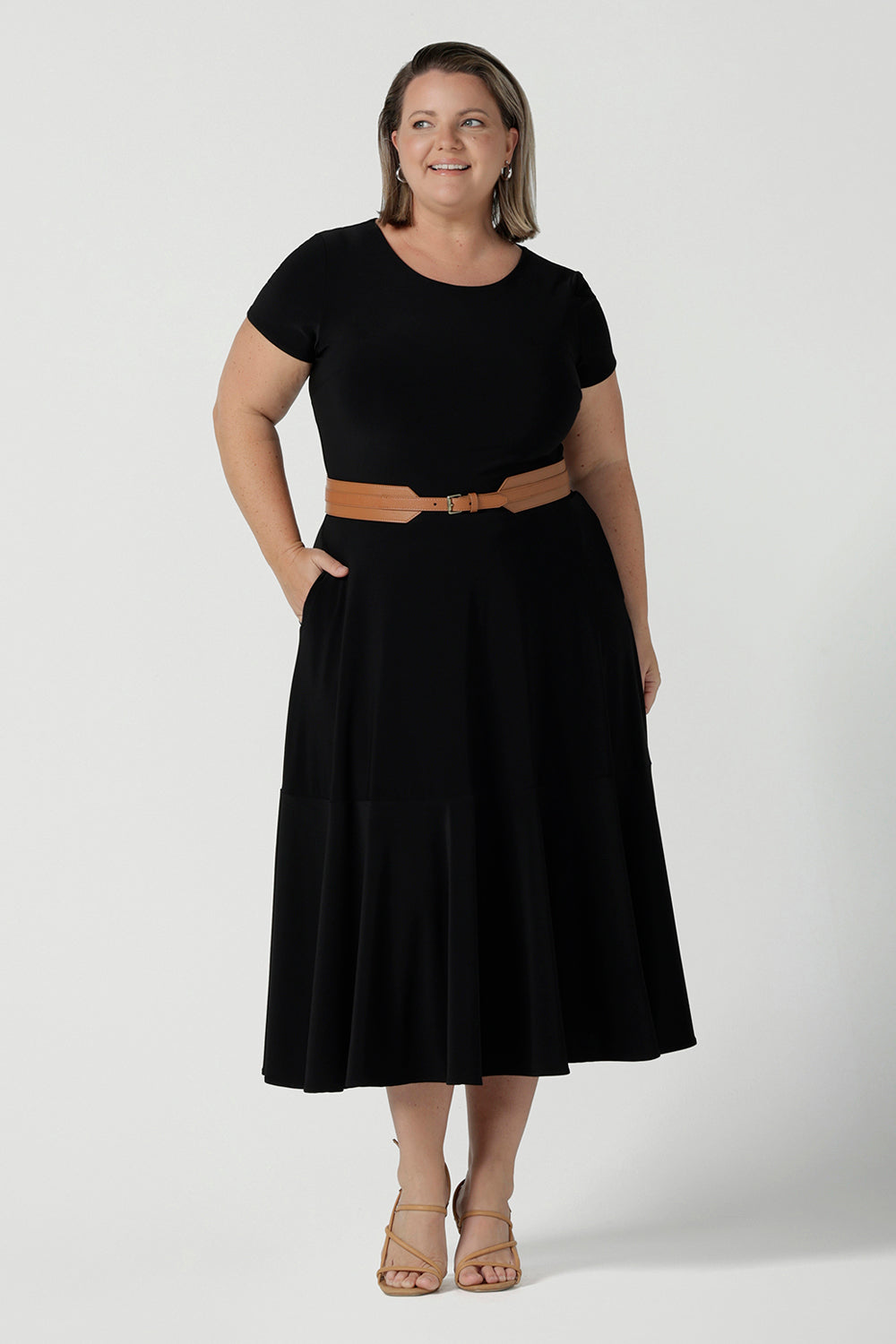 A size 18 woman wears the Amal dress in black is a slim fit round neck dress with waist seam and tier at the bottom. Functioning pockets. Great for work or event occasions. Made in Australia. Styled back with a belt. Size inclusive fashion for women size 8 - 24.