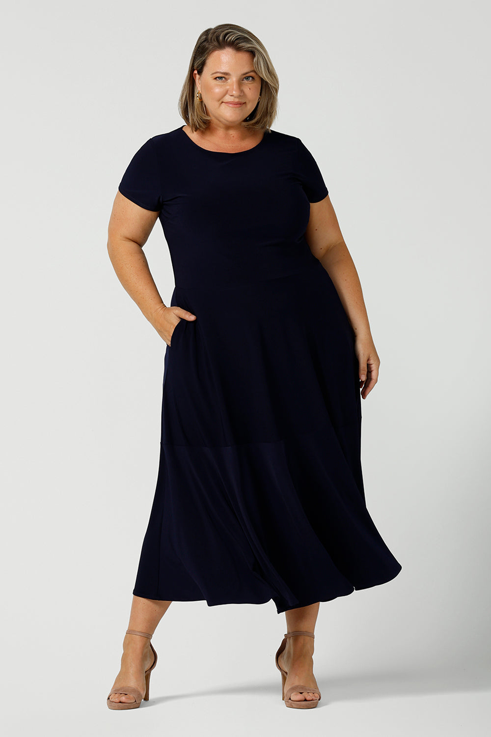If you're looking for dresses made in Australia, look to this elegant navy dress shown on a curvy, size 18 woman as a plus size dress. This high neck, short sleeve dress with flared skirt and ruffle hemline is a good workwear dress as well as a classic cocktail dress. With a midi-length skirt, shop this dress in plus sizes as well as petite thanks to made-in-Australia ladies clothing brand, Leina & Fleur.